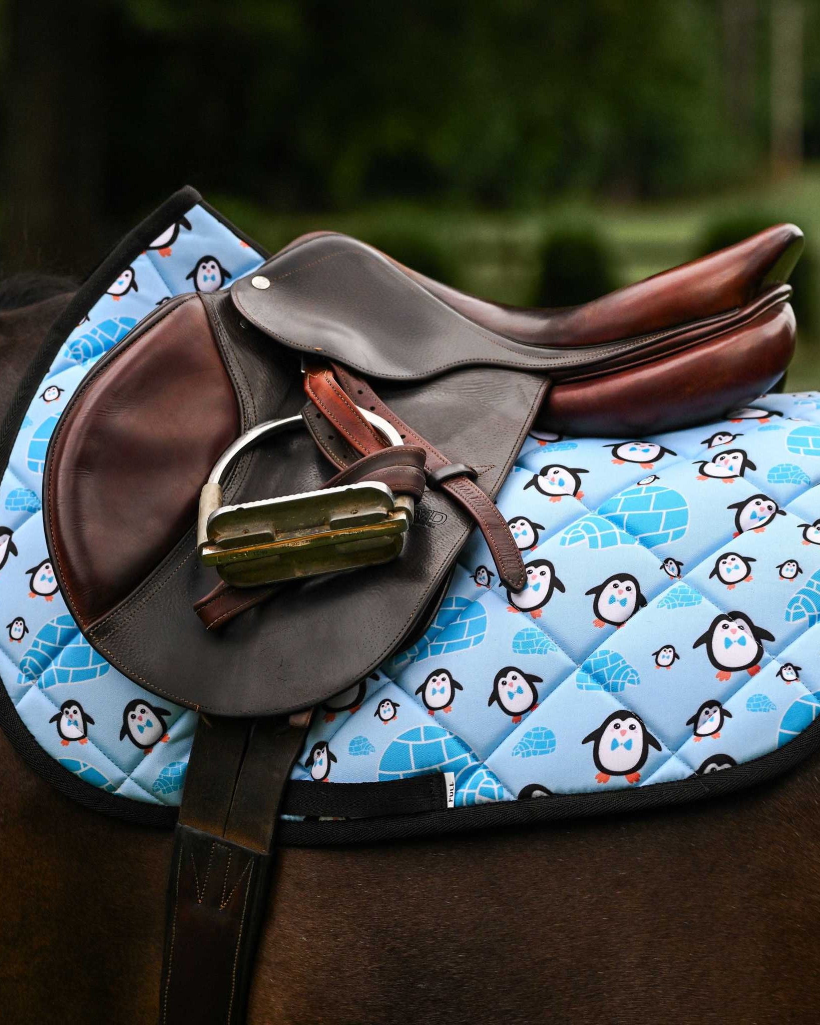 Igloo Crew Saddle Pad with penguin and igloo pattern under brown leather saddle on horse