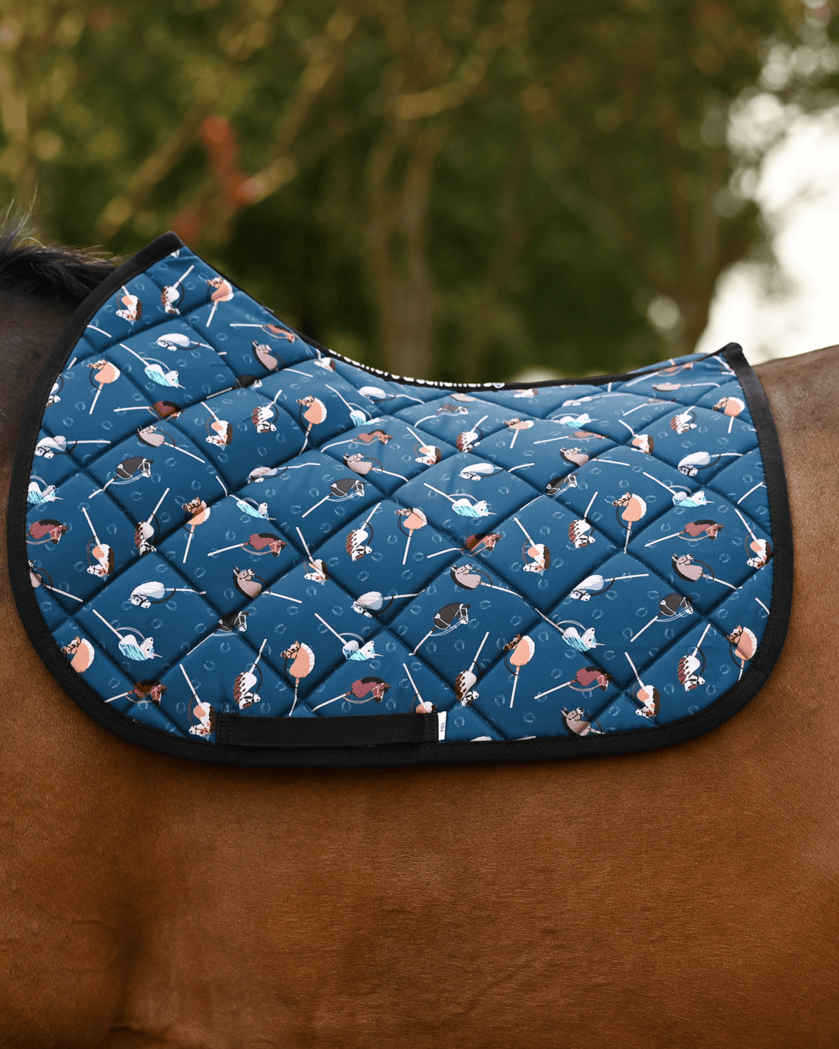 It's Not a Hobby saddle pad in dark teal, printed with stick hobby horses, shown bare on a bay horse