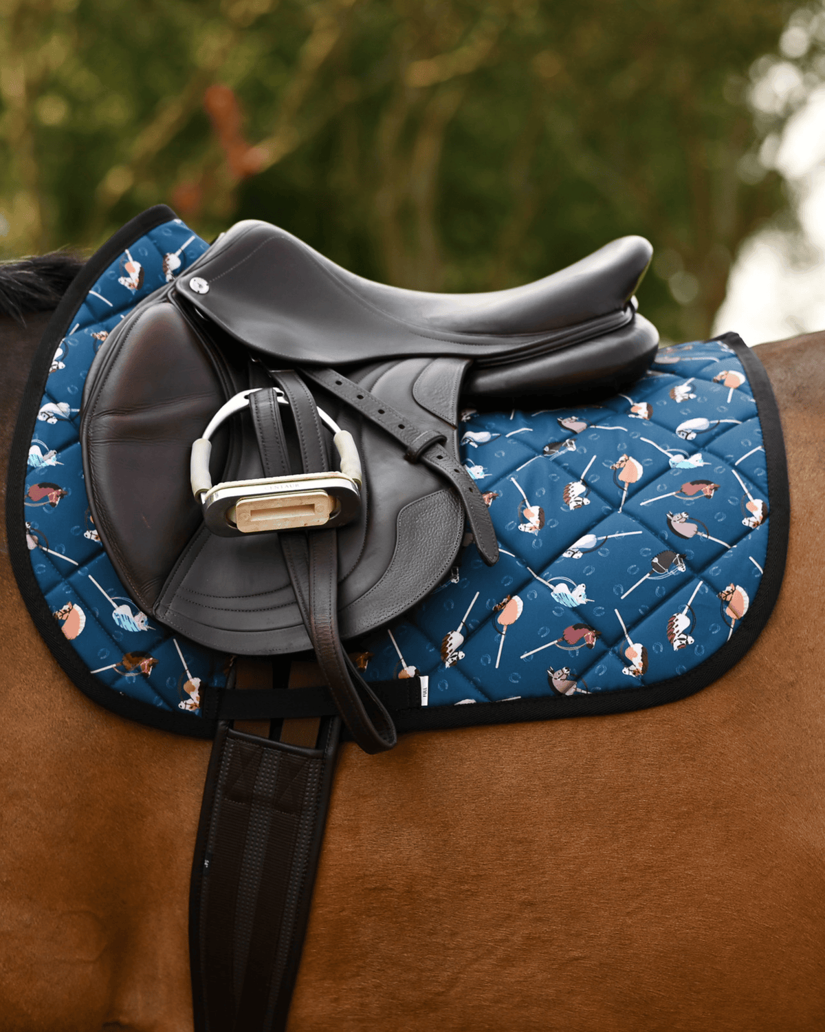Side profile of the It's Not a Hobby saddle pad in dark teal beneath a brown jumping saddle