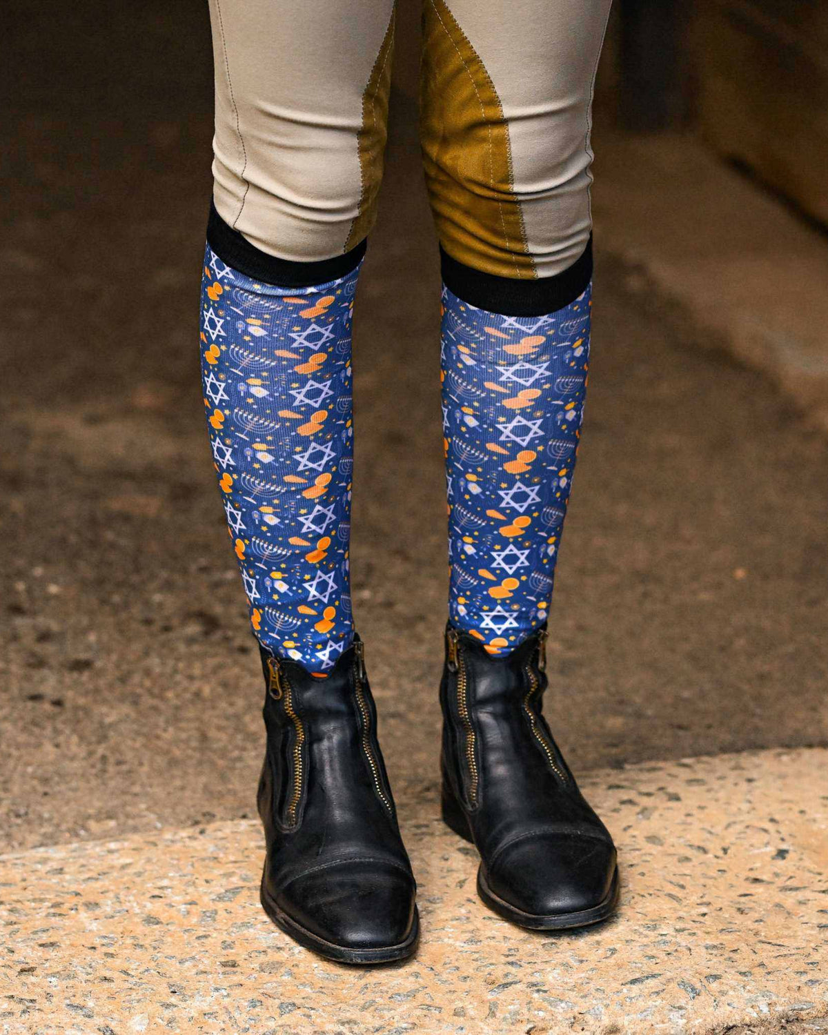 Blue "Keep Calm & Dreidel On" riding socks with Star of David and dreidel pattern worn with riding boots and beige breeches