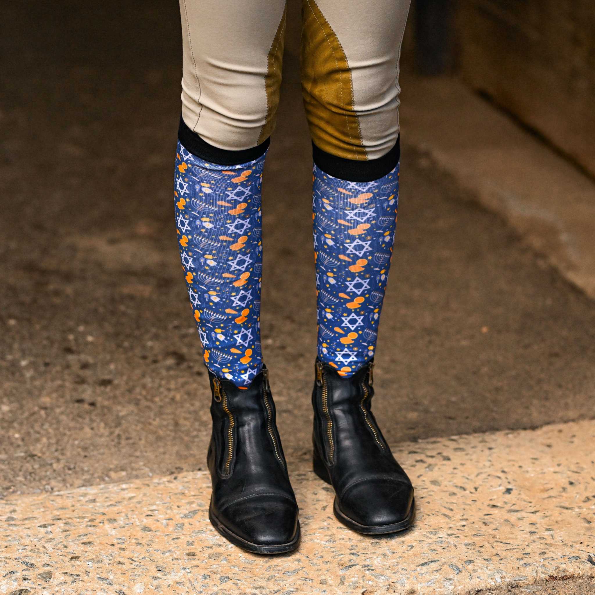 Blue "Keep Calm & Dreidel On" riding socks with Star of David and dreidel pattern worn with riding boots and beige breeches
