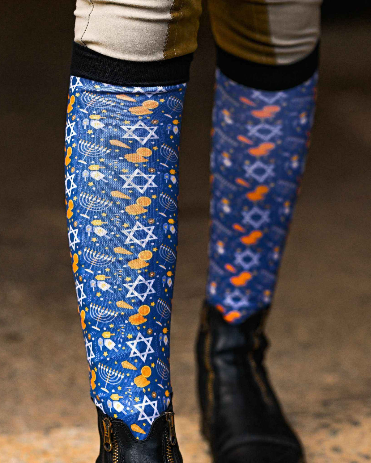 Hanukkah themed riding socks with Star of David and dreidel patterns, black top band, worn with riding boots