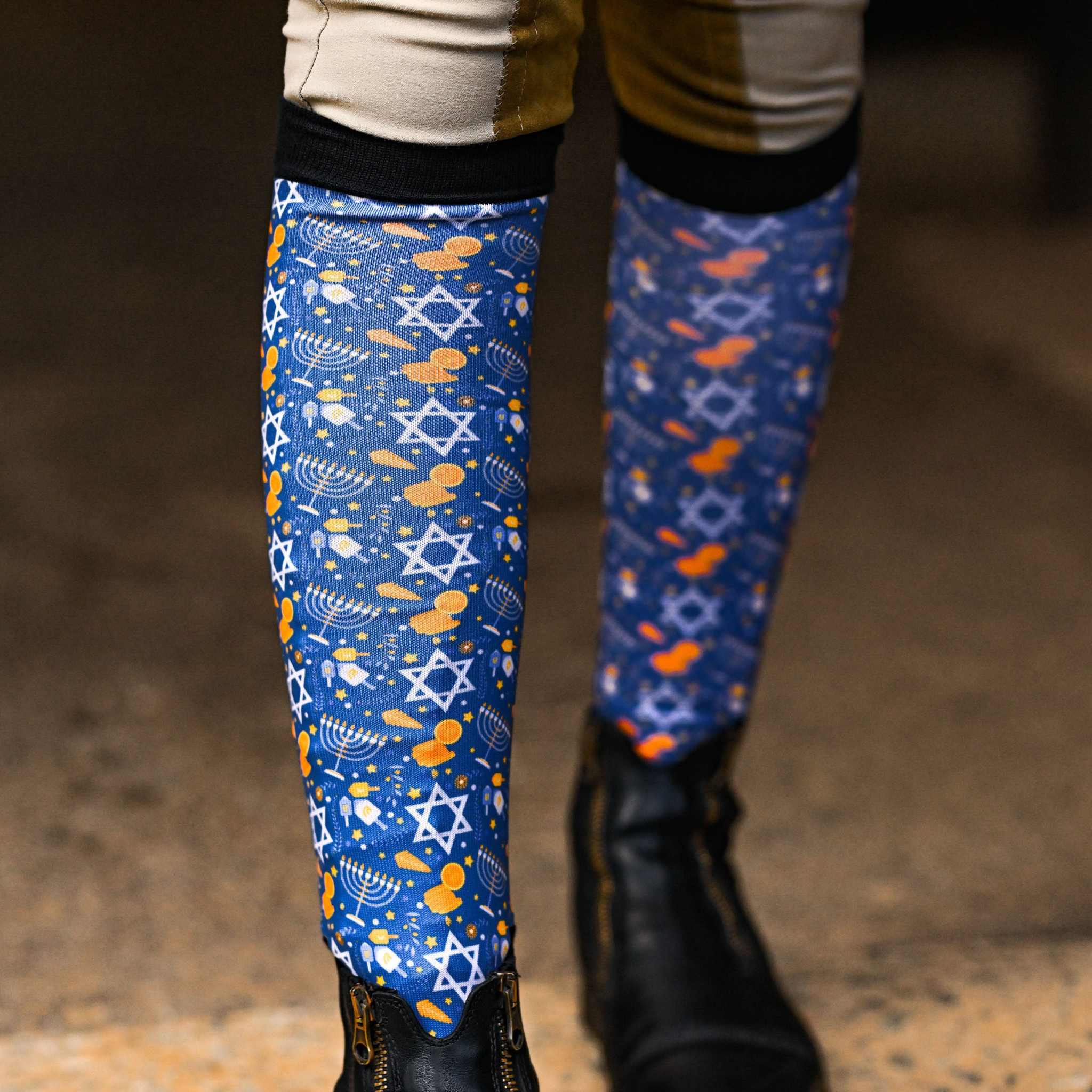 Hanukkah themed riding socks with Star of David and dreidel patterns, black top band, worn with riding boots