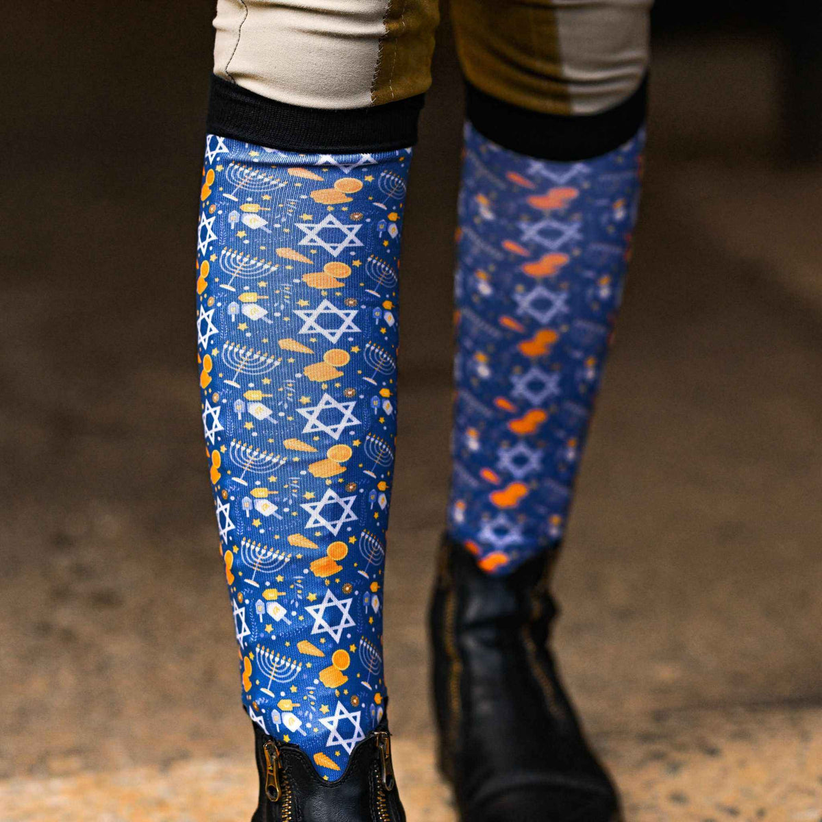 Hanukkah themed riding socks with Star of David and dreidel patterns, black top band, worn with riding boots