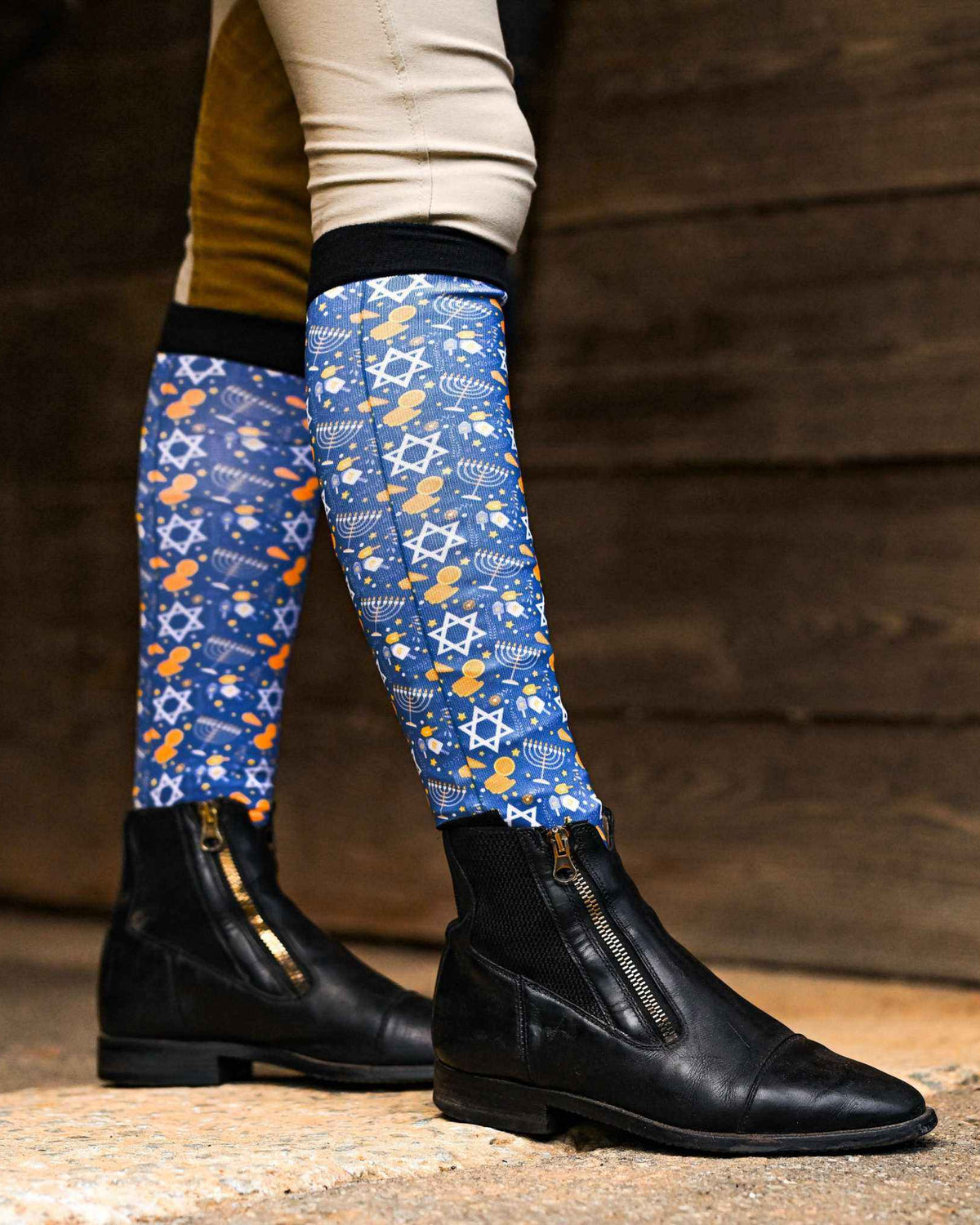 Blue Hanukkah-themed riding socks with dreidel and star patterns worn with black riding boots
