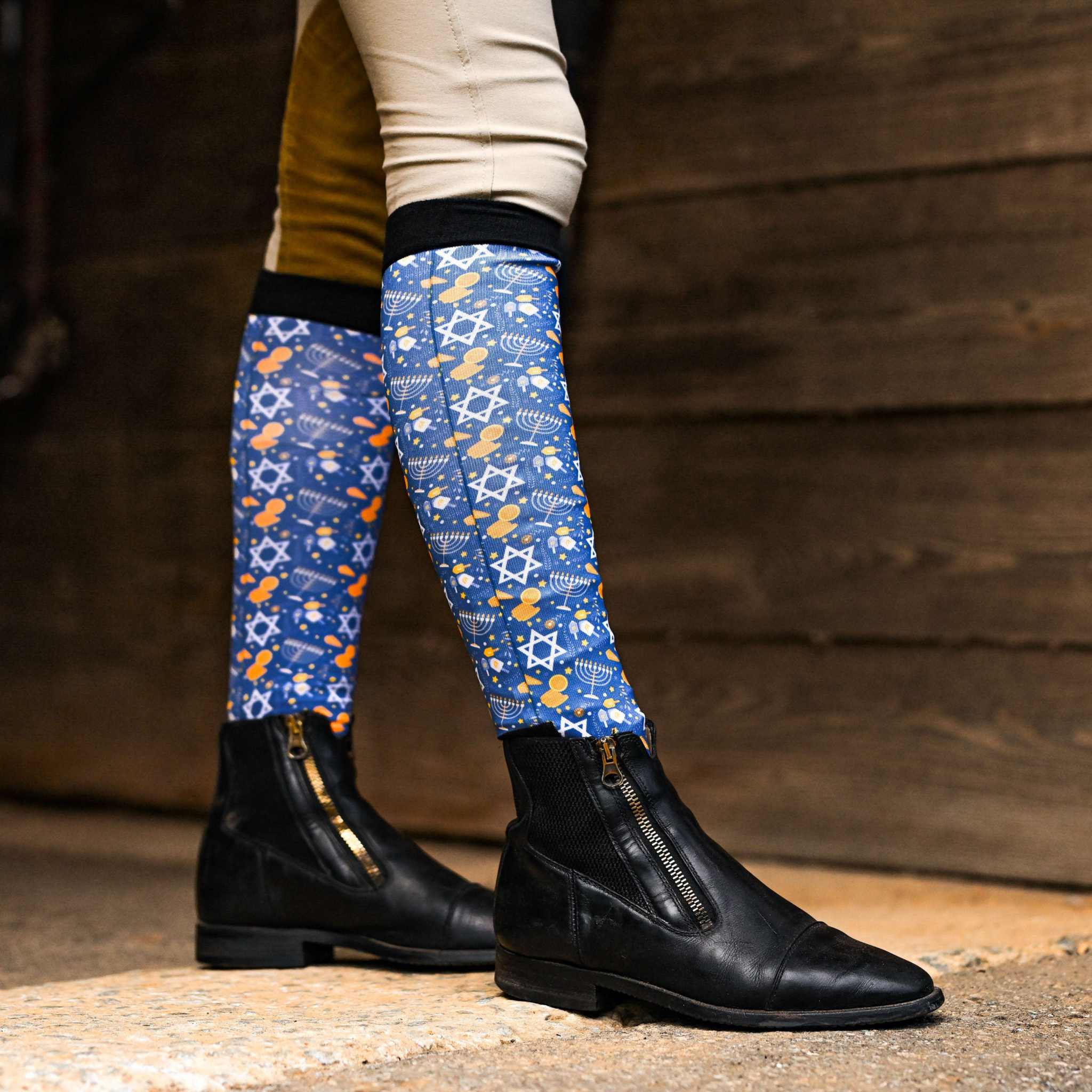 Blue Hanukkah-themed riding socks with dreidel and star patterns worn with black riding boots