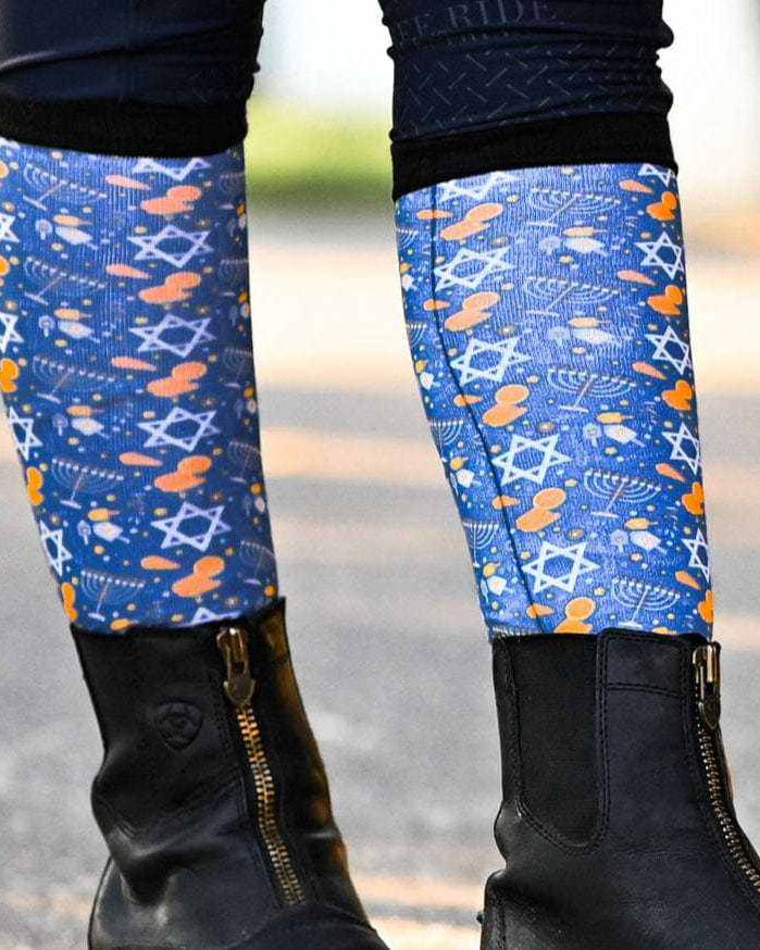Keep Calm & Dreidel On holiday-themed blue riding socks with menorahs and Stars of David worn with black boots