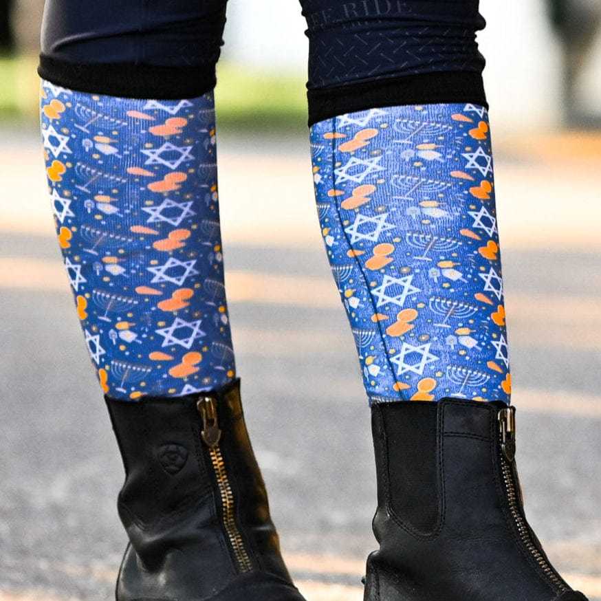 Keep Calm & Dreidel On holiday-themed blue riding socks with menorahs and Stars of David worn with black boots