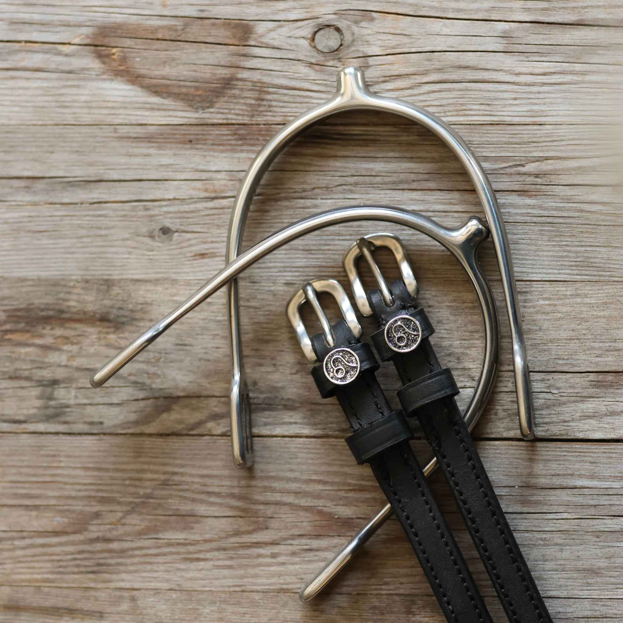 Black leather Leo Spur Straps with stainless steel buckles and custom ManeJane charms on wooden background
