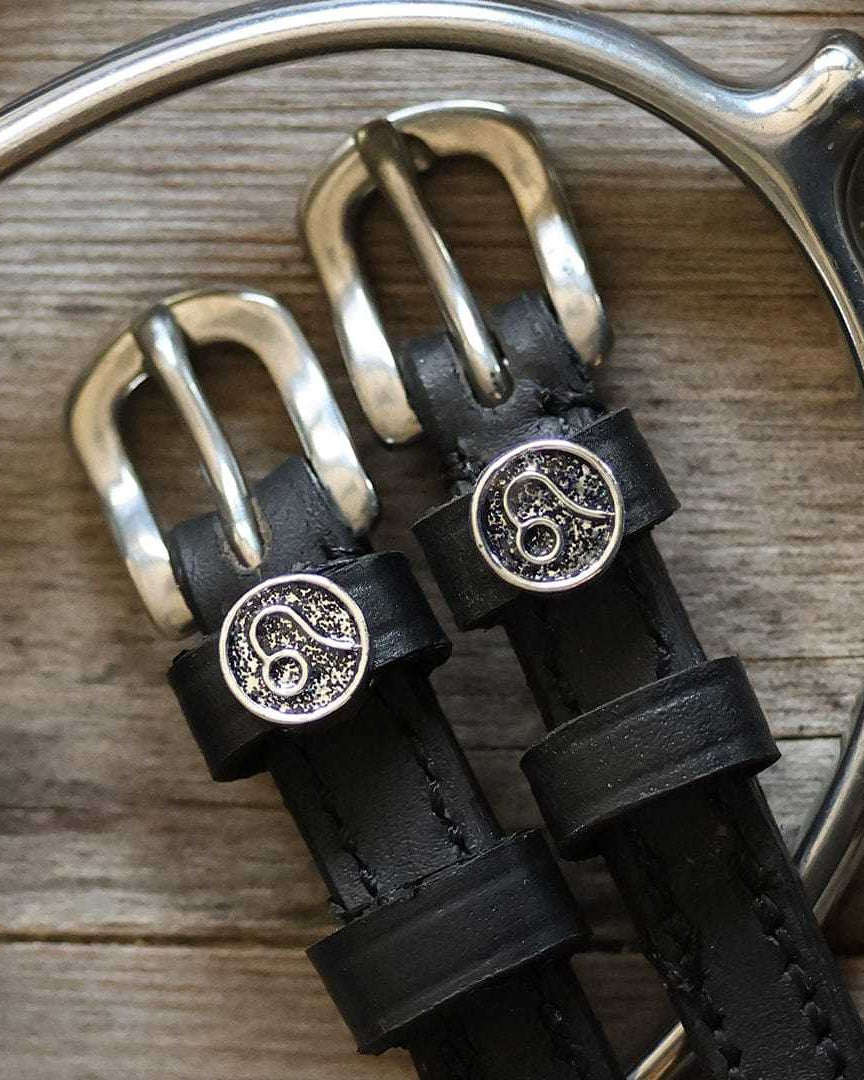 Black leather Leo Spur Straps with stainless steel buckle and custom charm on wooden background