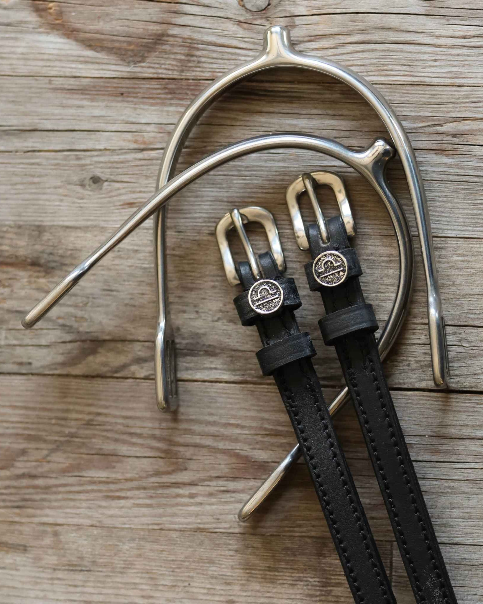 Libra Spur Straps black leather with stainless steel buckles and custom charm on wooden background