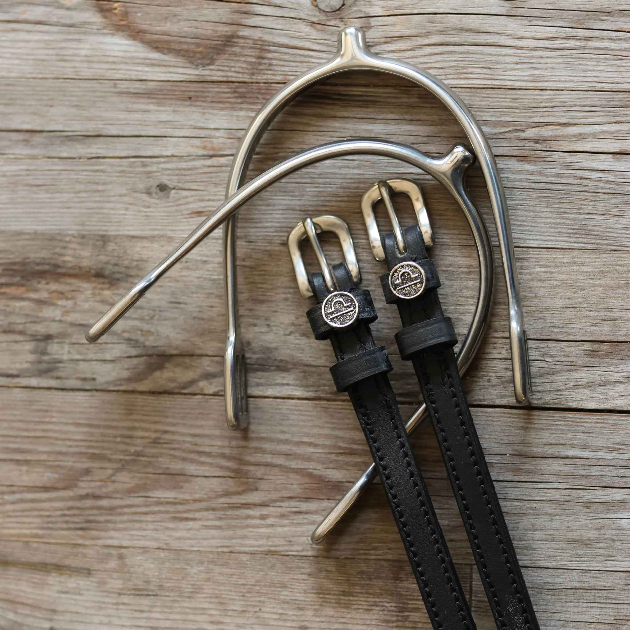 Libra Spur Straps black leather with stainless steel buckles and custom charm on wooden background