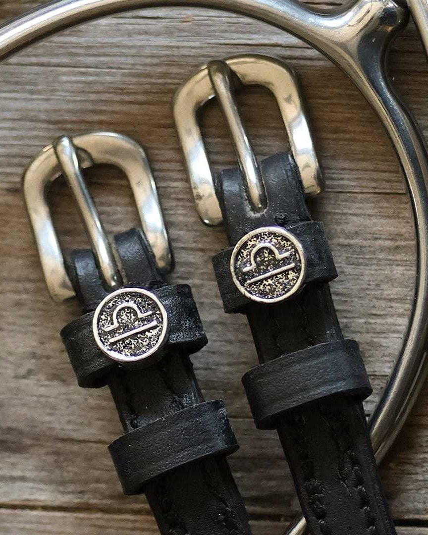 Black leather Libra Spur Straps with silver buckles and custom Libra charm on wooden background