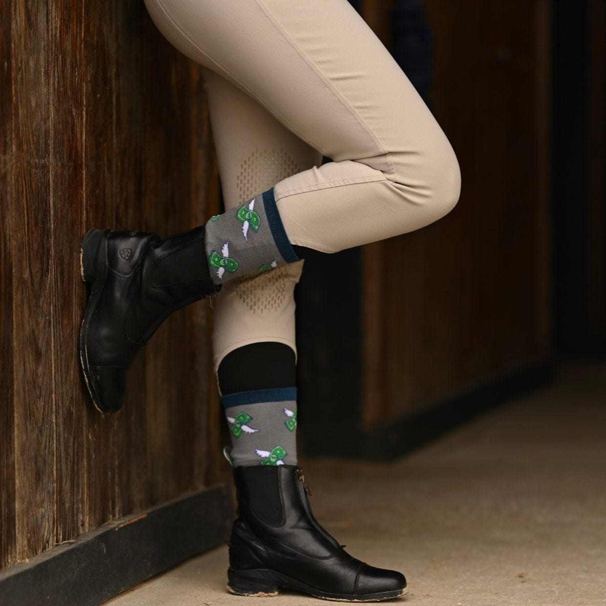 Equestrian with beige riding pants and black boots wearing grey socks with green flying money design from Manifesting Money Bundle