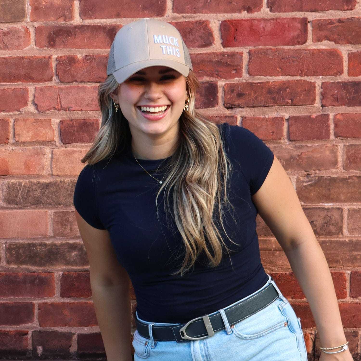 Woman wearing Muck This trucker hat, navy shirt, and jeans against brick wall