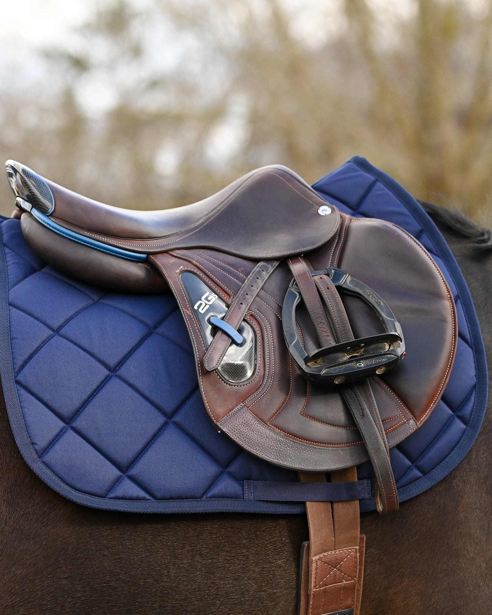 Blue equestrian bundle featuring navy saddle pad, brown leather saddle, and blue ribbon spur straps on horse