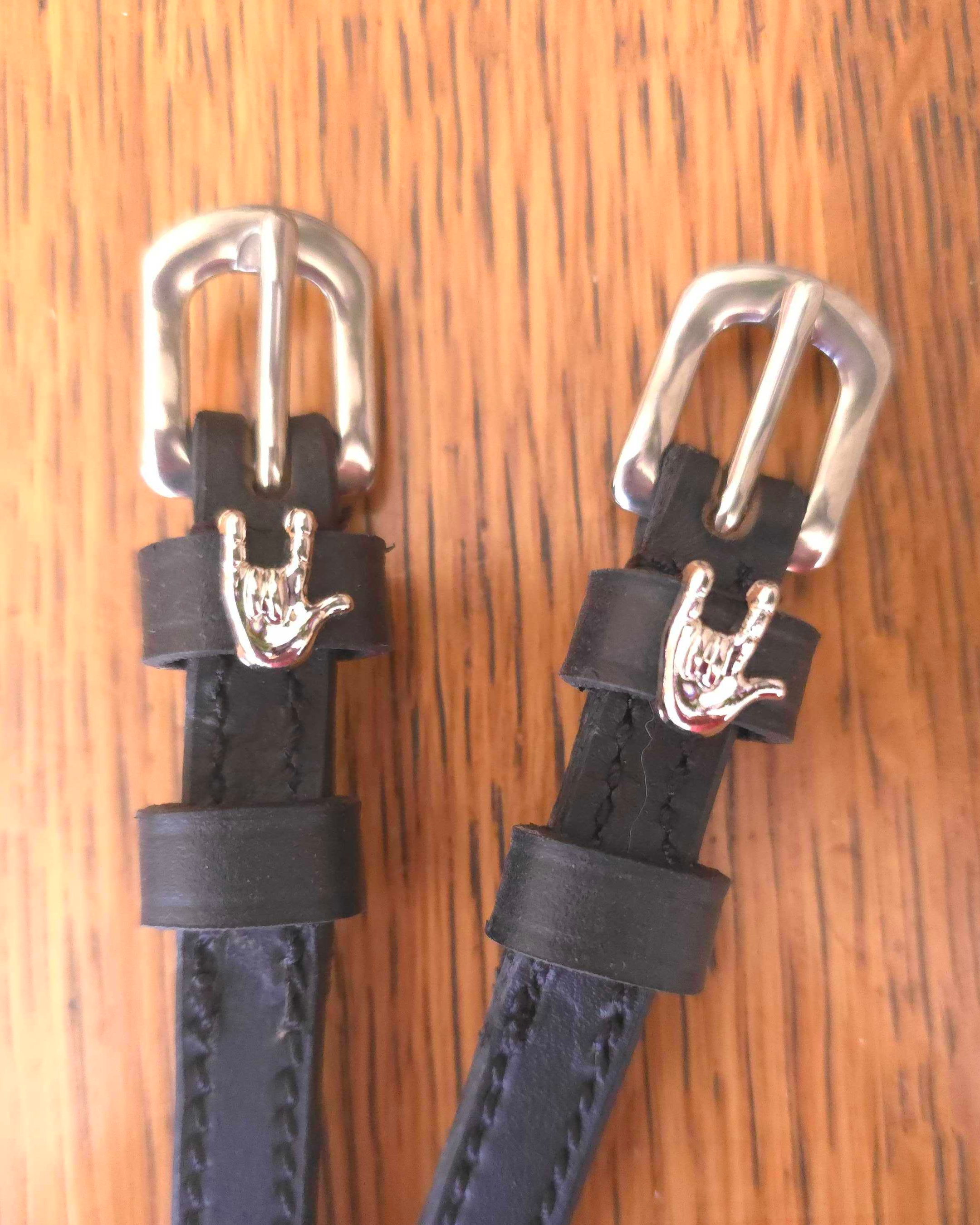 Pair of black leather ManeJane spur straps with silver rock-on hand charms on wood