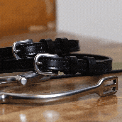 Not So Basic Black equestrian gift bundle with black leather spur straps and stainless steel buckle on wooden surface