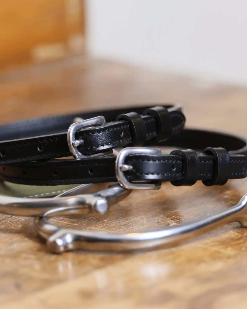 Close-up of black leather spur straps with stainless steel buckles and metal spurs on wooden surface from Not So Basic Black equestrian gift bundle