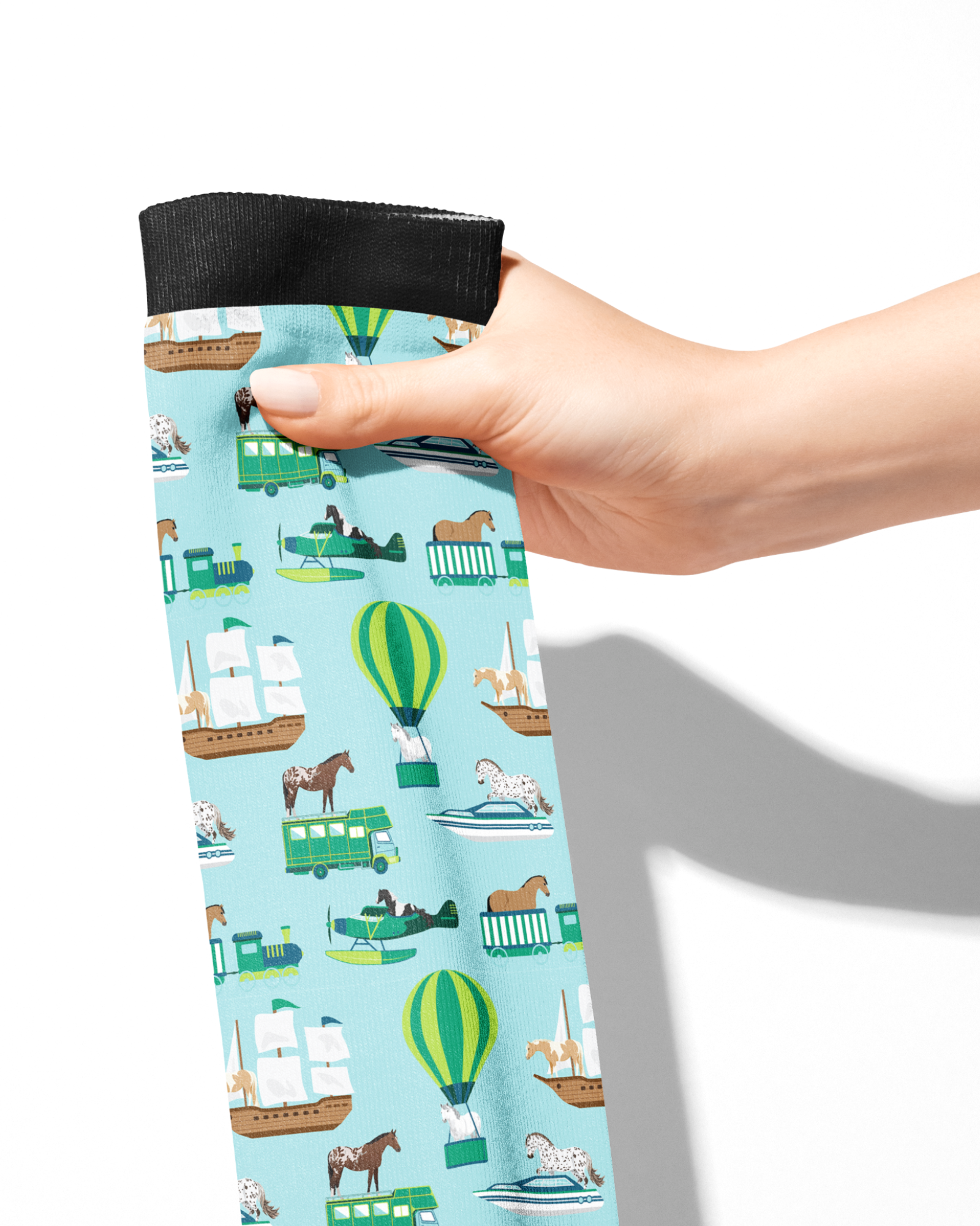 Hand holding Limited Edition Pony Island Pony Transport Socks with pony and transport vehicle design on light blue background