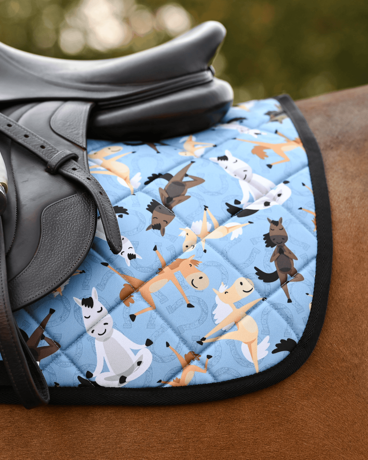 Pony Pilates pad in denim blue with black binding, shown under a black dressage saddle on a bay horse