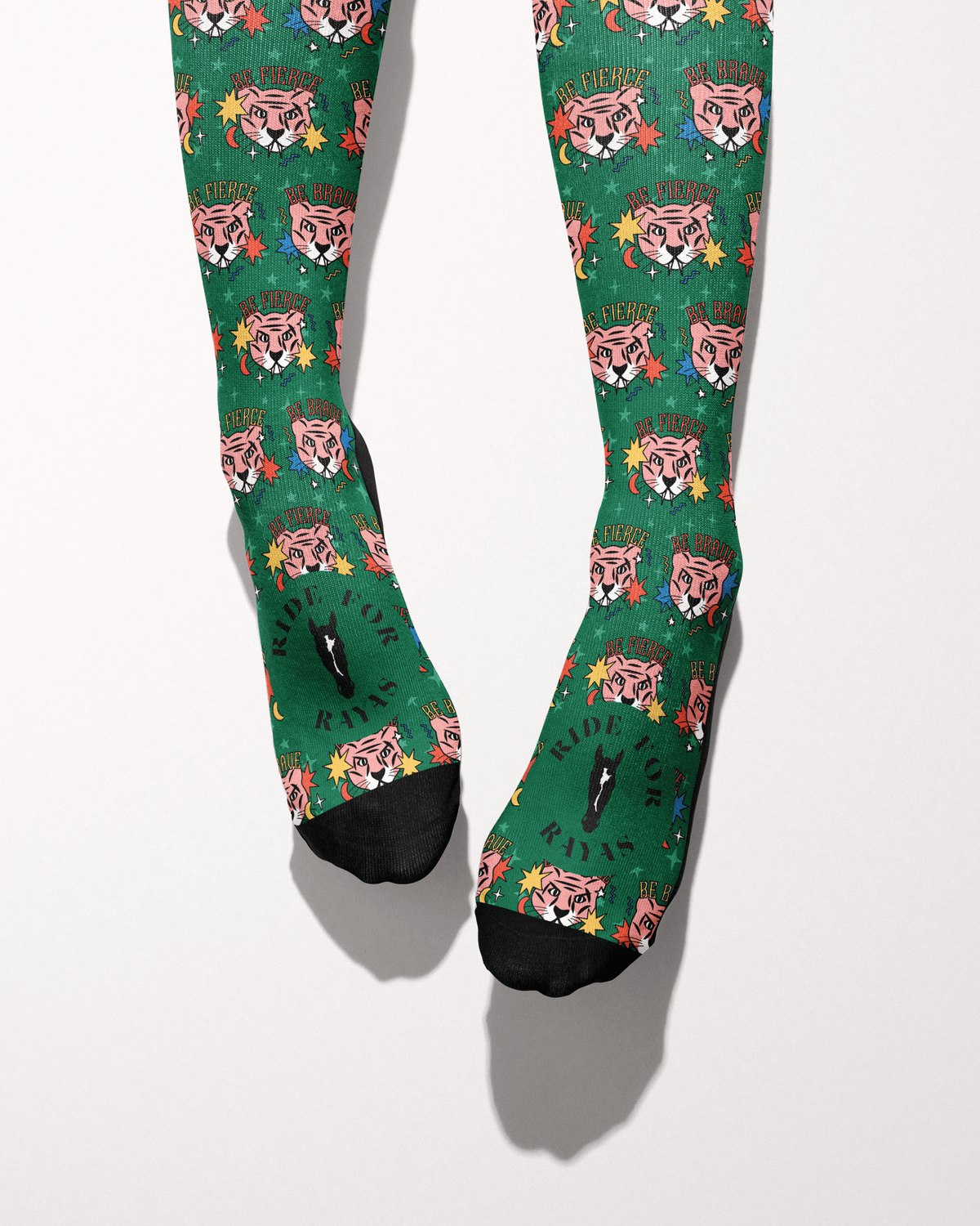 Be Brave socks seen from the toes, black toe caps and the Ride for Rayas horse logo on the green tiger print