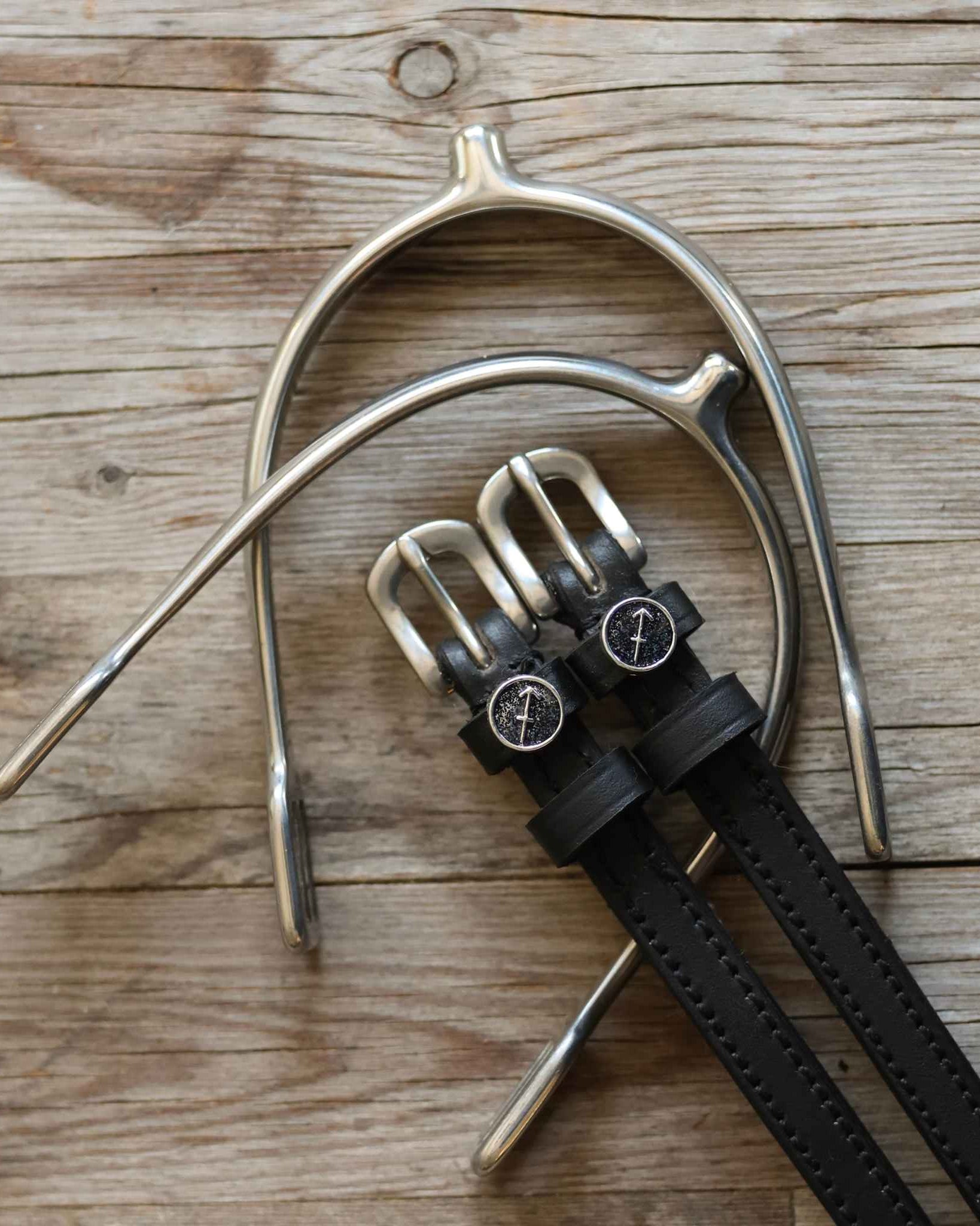 Black leather Sagittarius Spur Straps with stainless steel buckles and custom charms on wooden background