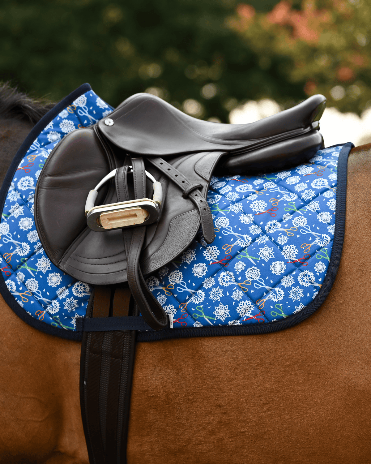 Side view of the Shear Magic saddle pad beneath a brown jumping saddle and stirrup on a bay horse