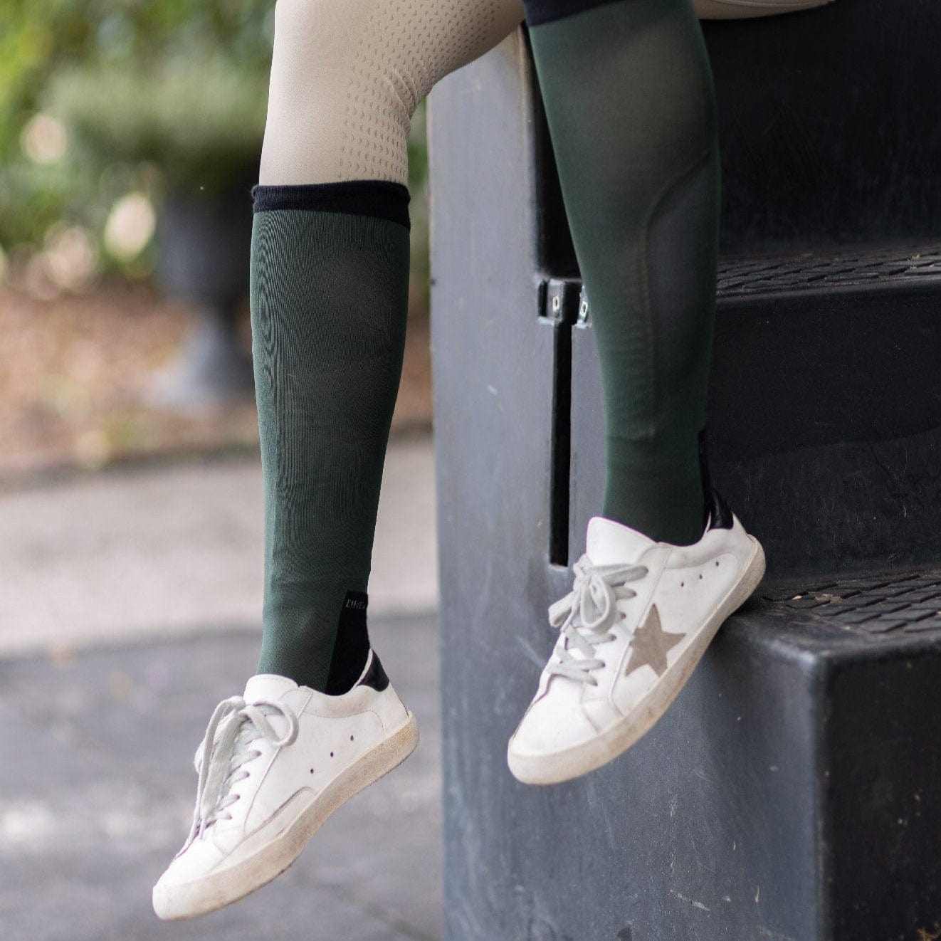 Equestrian wearing hunter green socks from Manifesting Money Bundle with white sneakers sitting on stairs