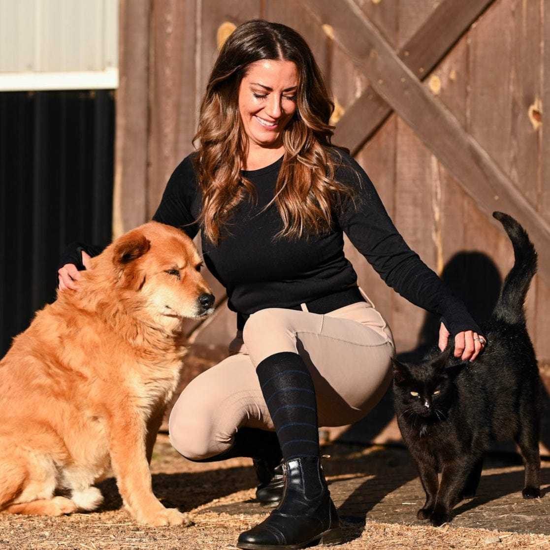 woman wearing knit boot socks with black stripes playing with a dog and a black cat outdoors