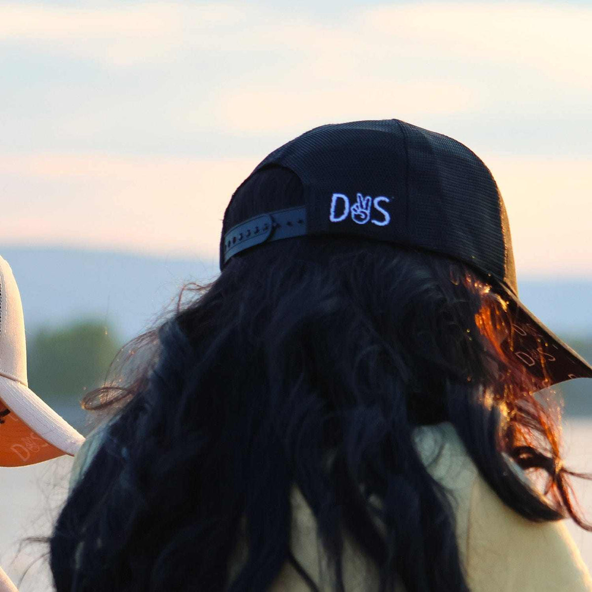 Stall Rest Equestrian Bundle black trucker hat worn by person with long hair outdoors at sunset