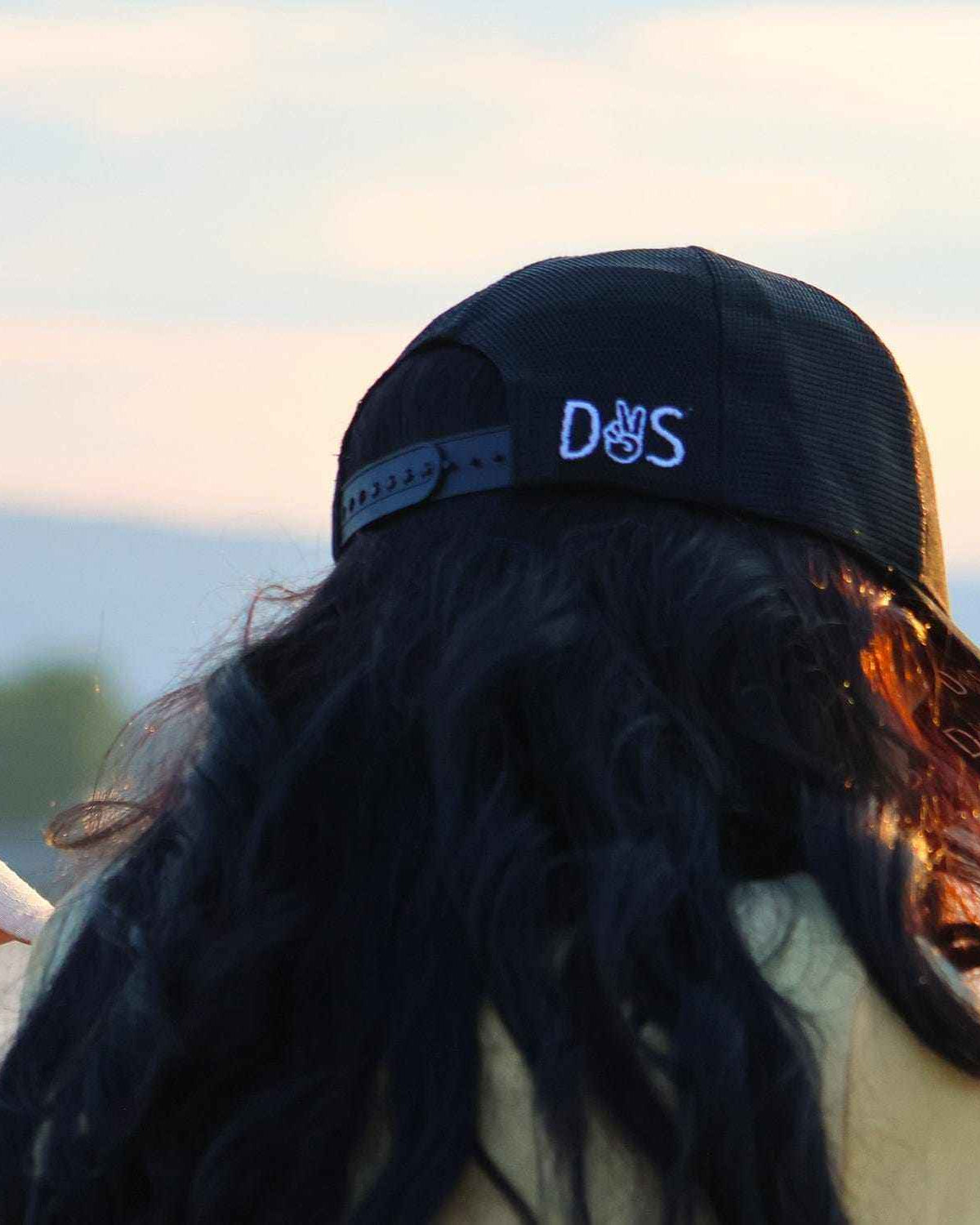 Stall Rest Equestrian Bundle black trucker hat worn by person with long hair outdoors at sunset