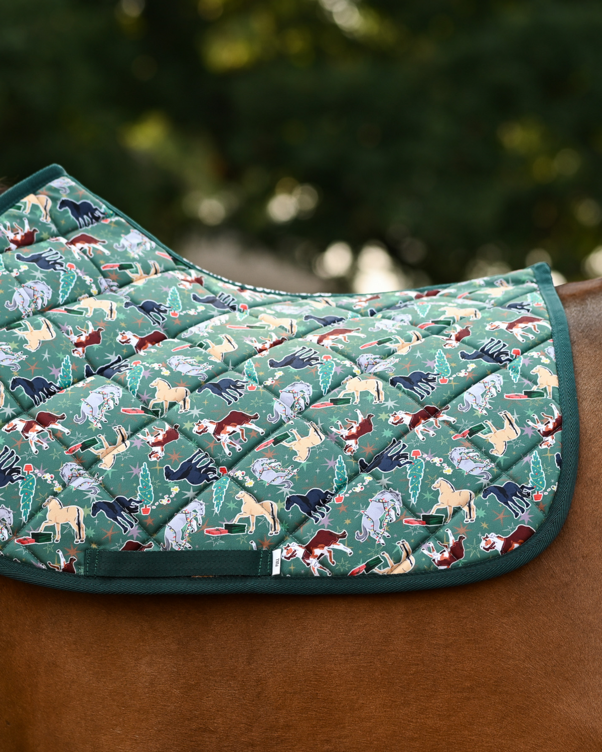Green Naughty List holiday pad with multi-coloured horses, trees and gifts, on a chestnut horse
