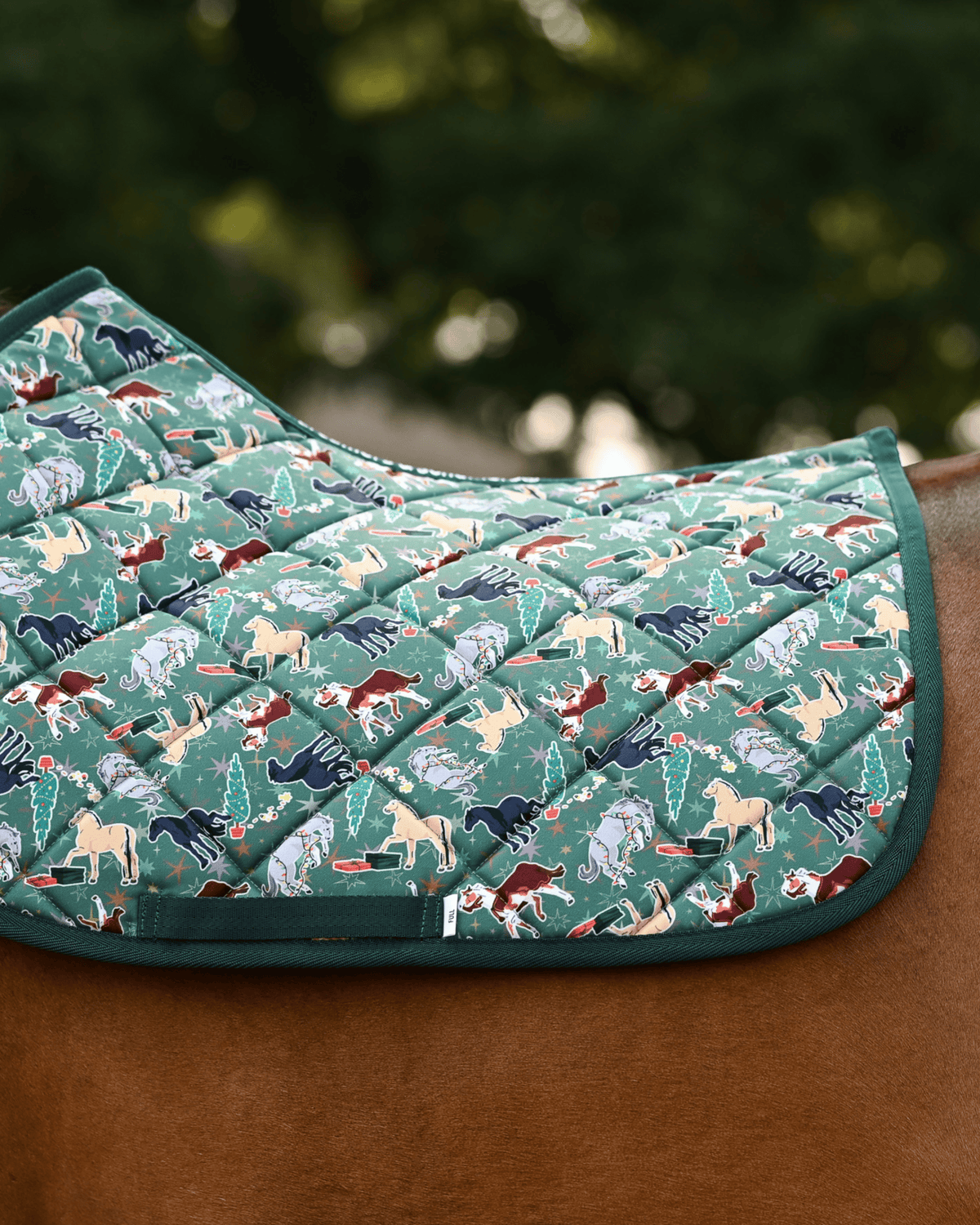 Green Naughty List holiday pad with multi-coloured horses, trees and gifts, on a chestnut horse