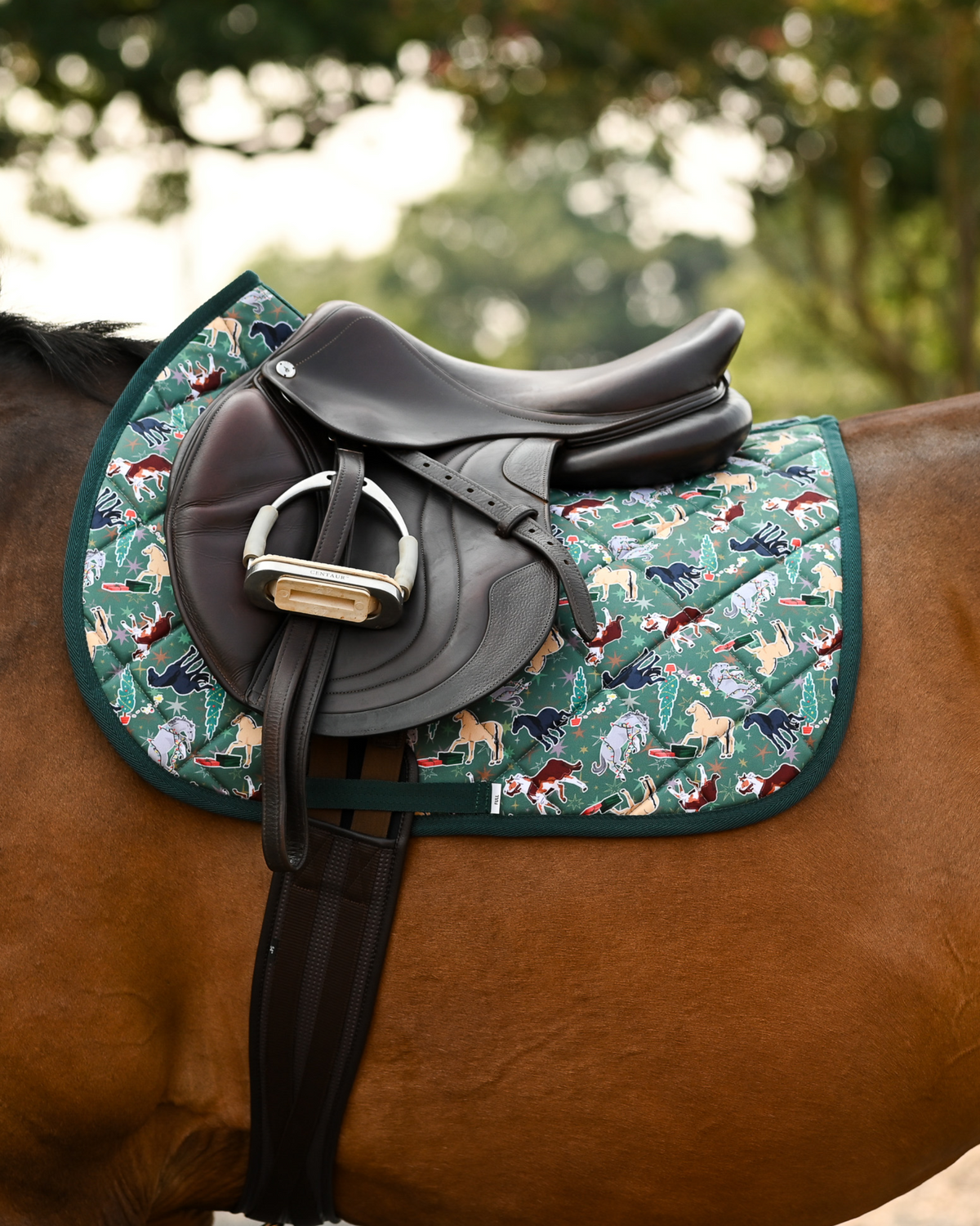 The Naughty List pad in green under a brown jumping saddle, forest green binding on a bay horse