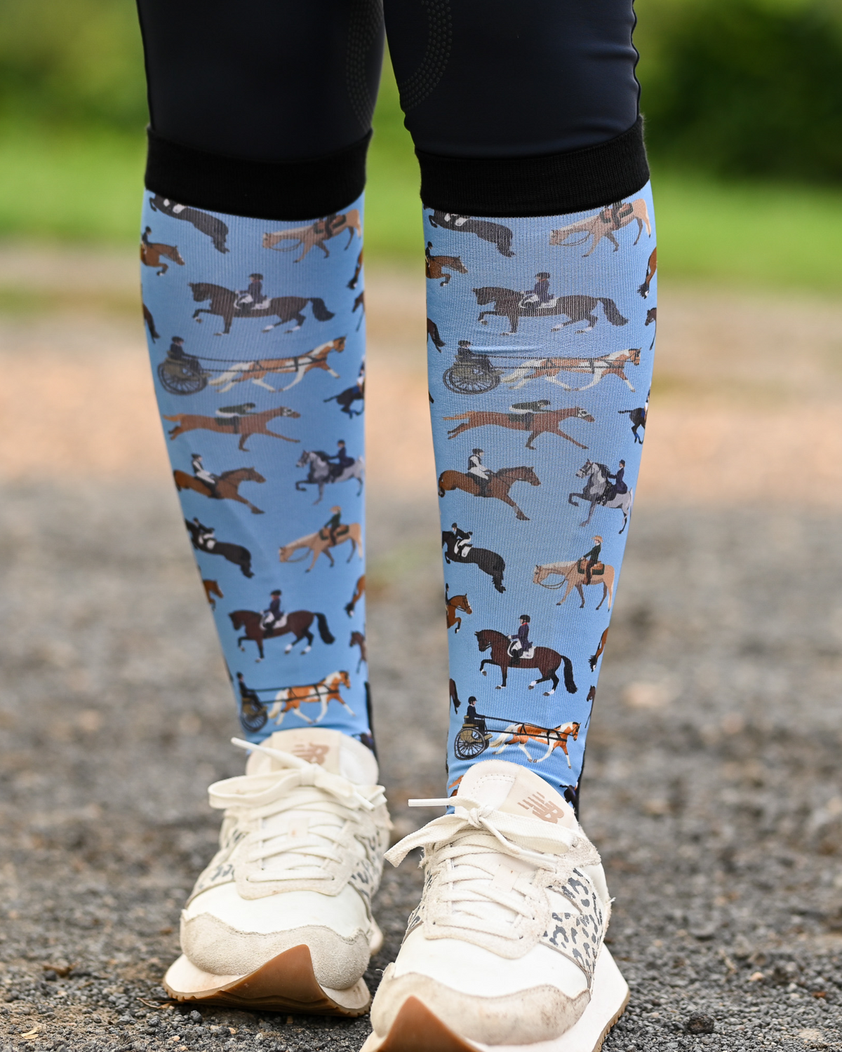 The Pony Island Horse Sports boot socks seen from the front, light blue ground scattered with riders mounted across every discipline