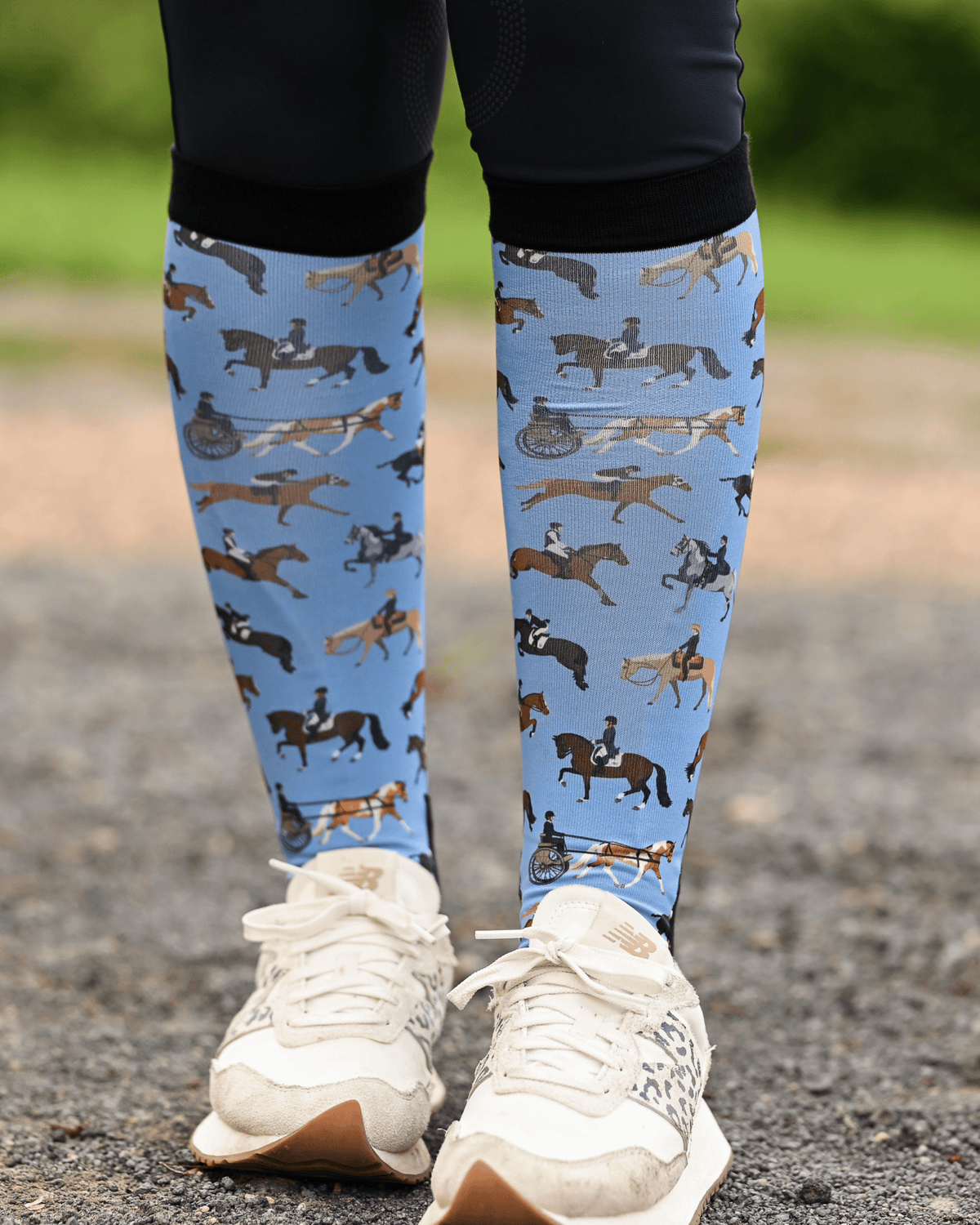The Pony Island Horse Sports boot socks seen from the front, light blue ground scattered with riders mounted across every discipline