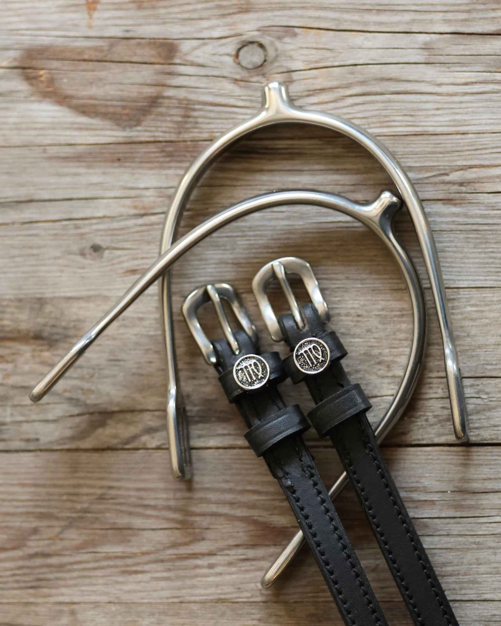 Virgo Spur Straps black leather with stainless steel buckles and custom Virgo charm on wooden background
