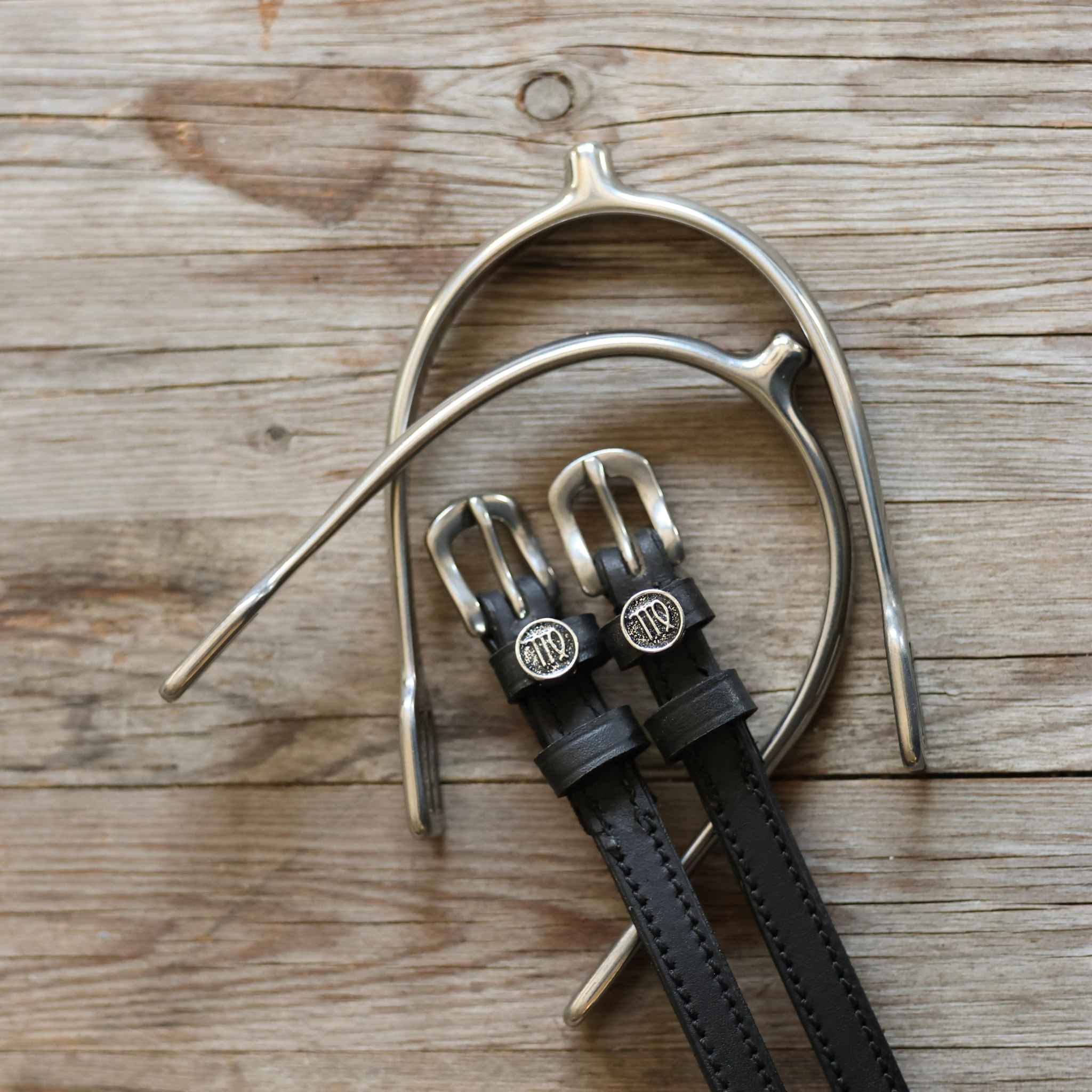 Virgo Spur Straps black leather with stainless steel buckles and custom Virgo charm on wooden background