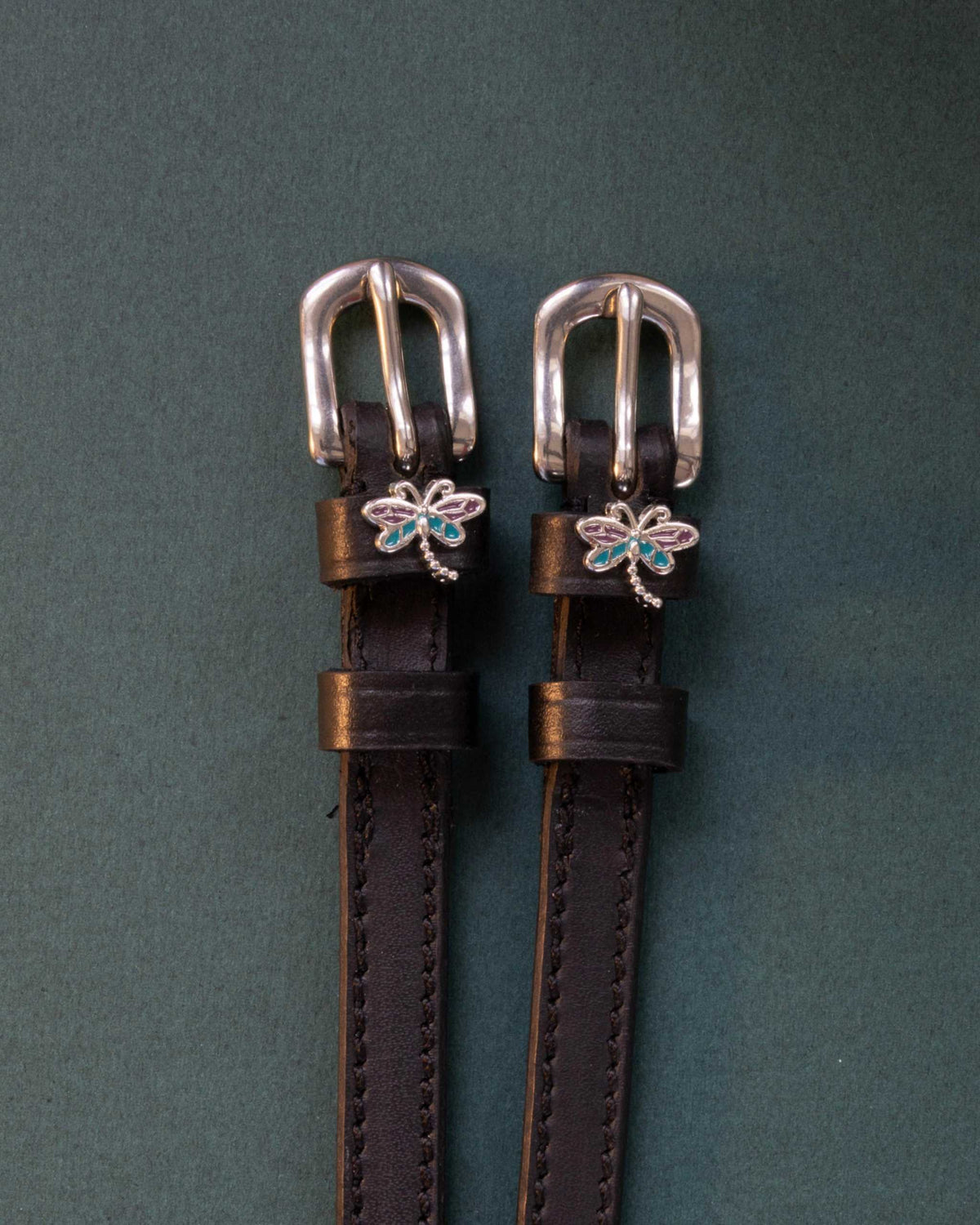 Dragonfly ManeJane spur straps with the signature Dragonfly charm, shown on a charcoal background