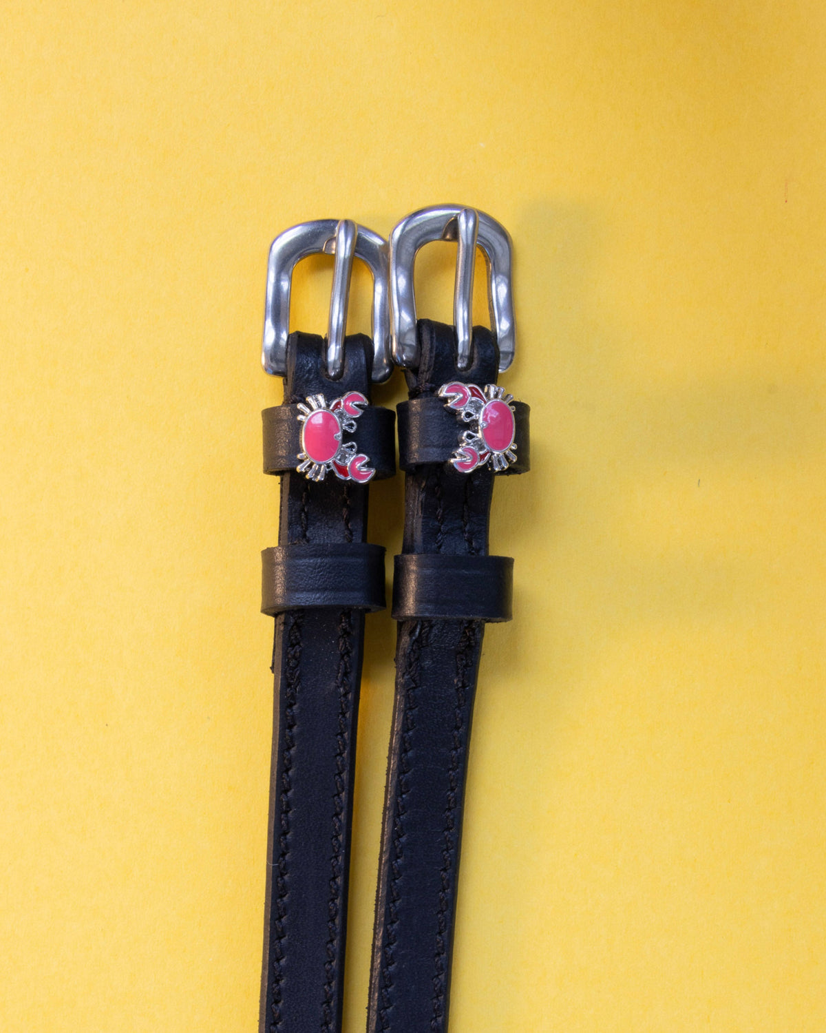 Pair of Crabbin' ManeJane spur straps, black leather with stainless buckles, on a yellow backdrop