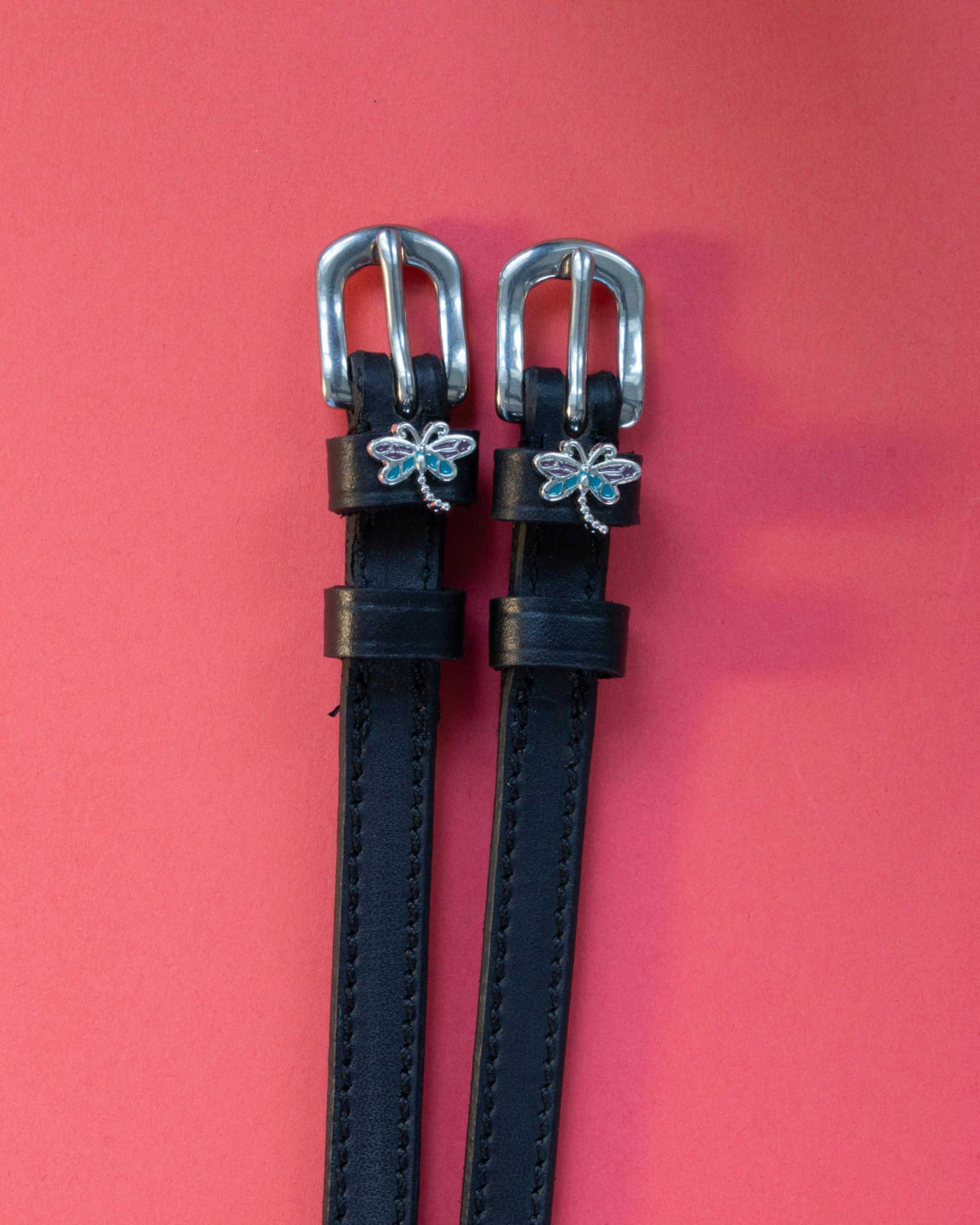 Dragonfly ManeJane spur straps with the signature Dragonfly charm, shown on a coral background