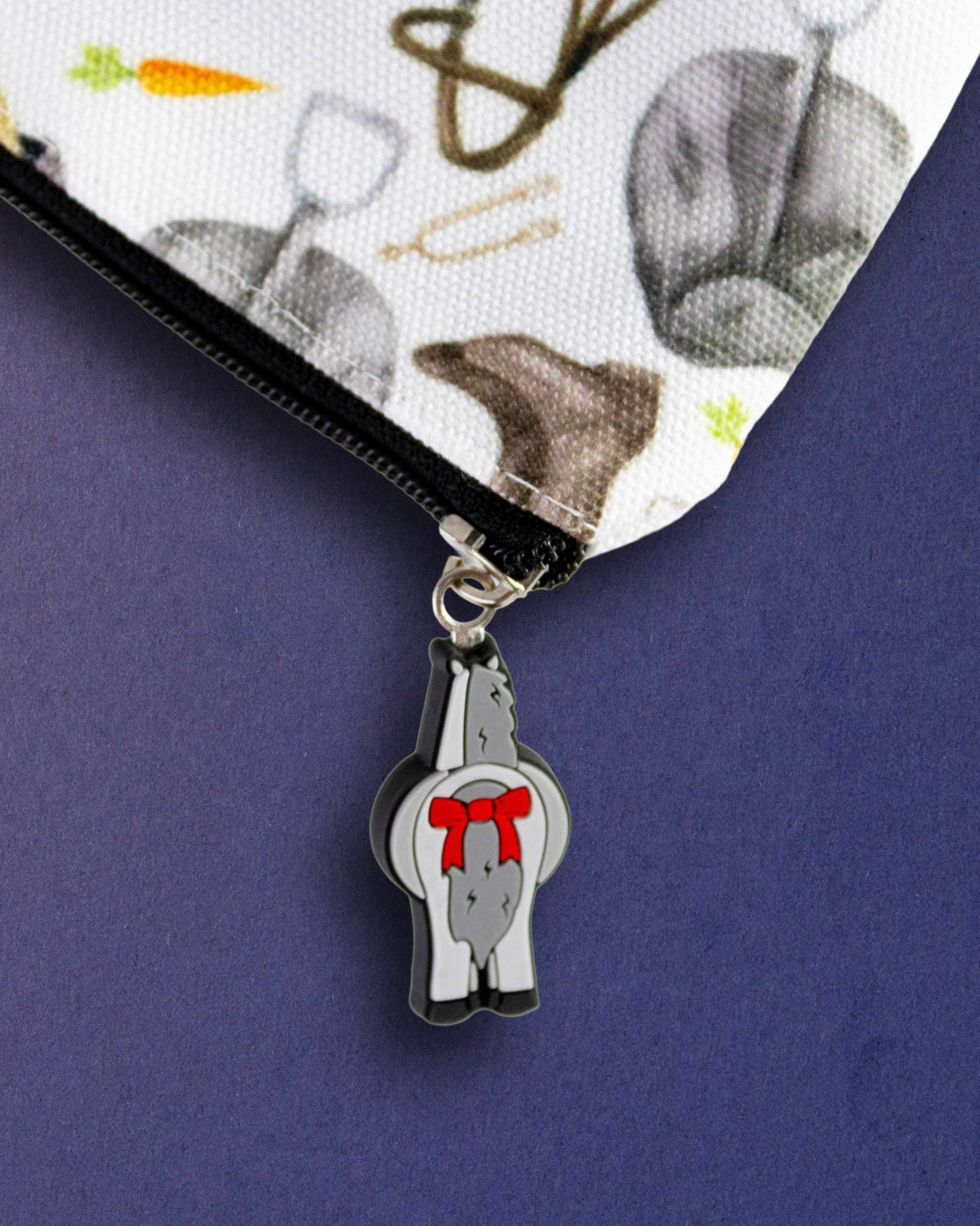 Close-up of the bad pony zip pull, a grey horse charm with a red bow, on The Hunt zip pouch