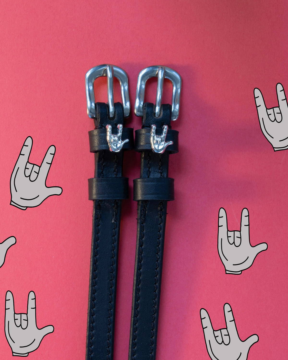Rock On ManeJane spur straps with the signature Rock On charm, shown on a coral background, by Dreamers & Schemers