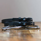 Black leather Chocolate Bar Spur Straps with stainless steel buckles and custom charm on wooden surface
