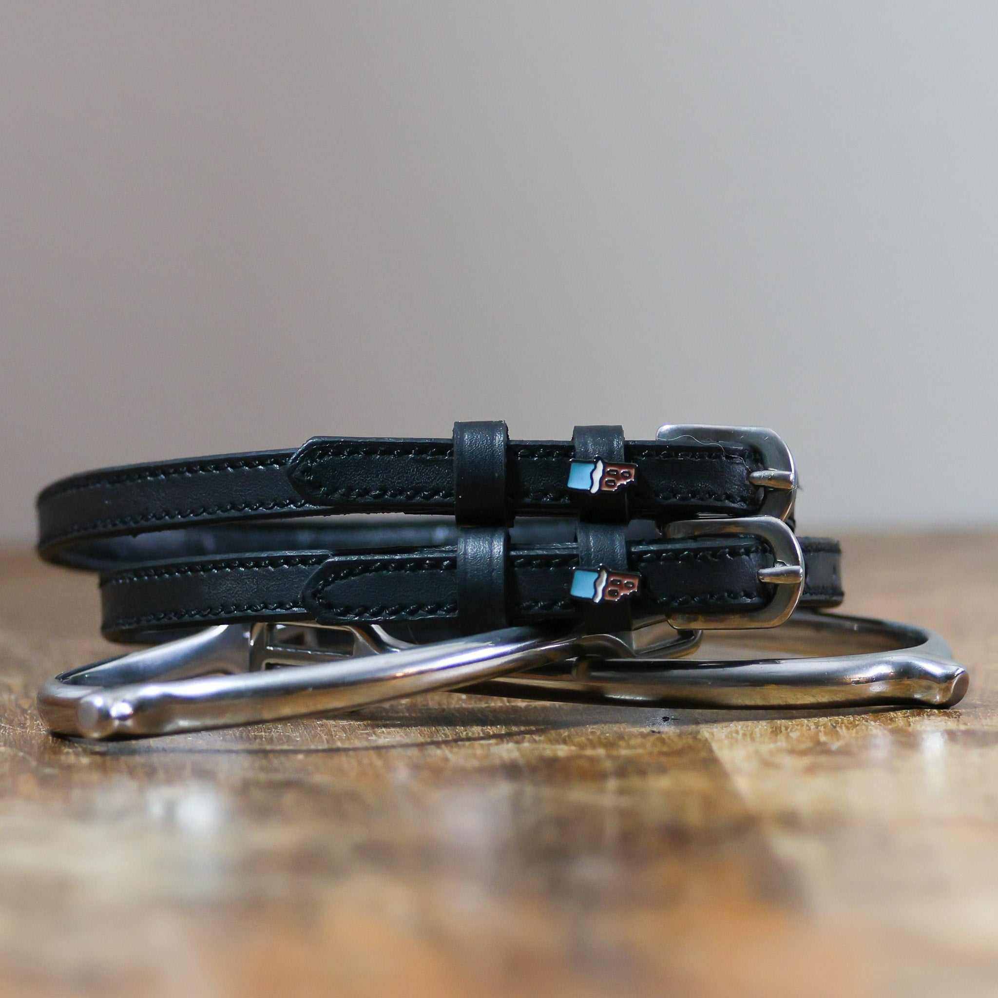 Black leather Chocolate Bar Spur Straps with stainless steel buckles and custom charm on wooden surface