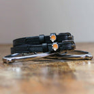 Black leather hedgehog spur straps with stainless steel buckles and custom charms on wooden surface