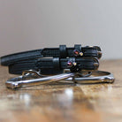 Black leather F Bomb Spur Straps with stainless steel buckles and custom charms on wooden surface