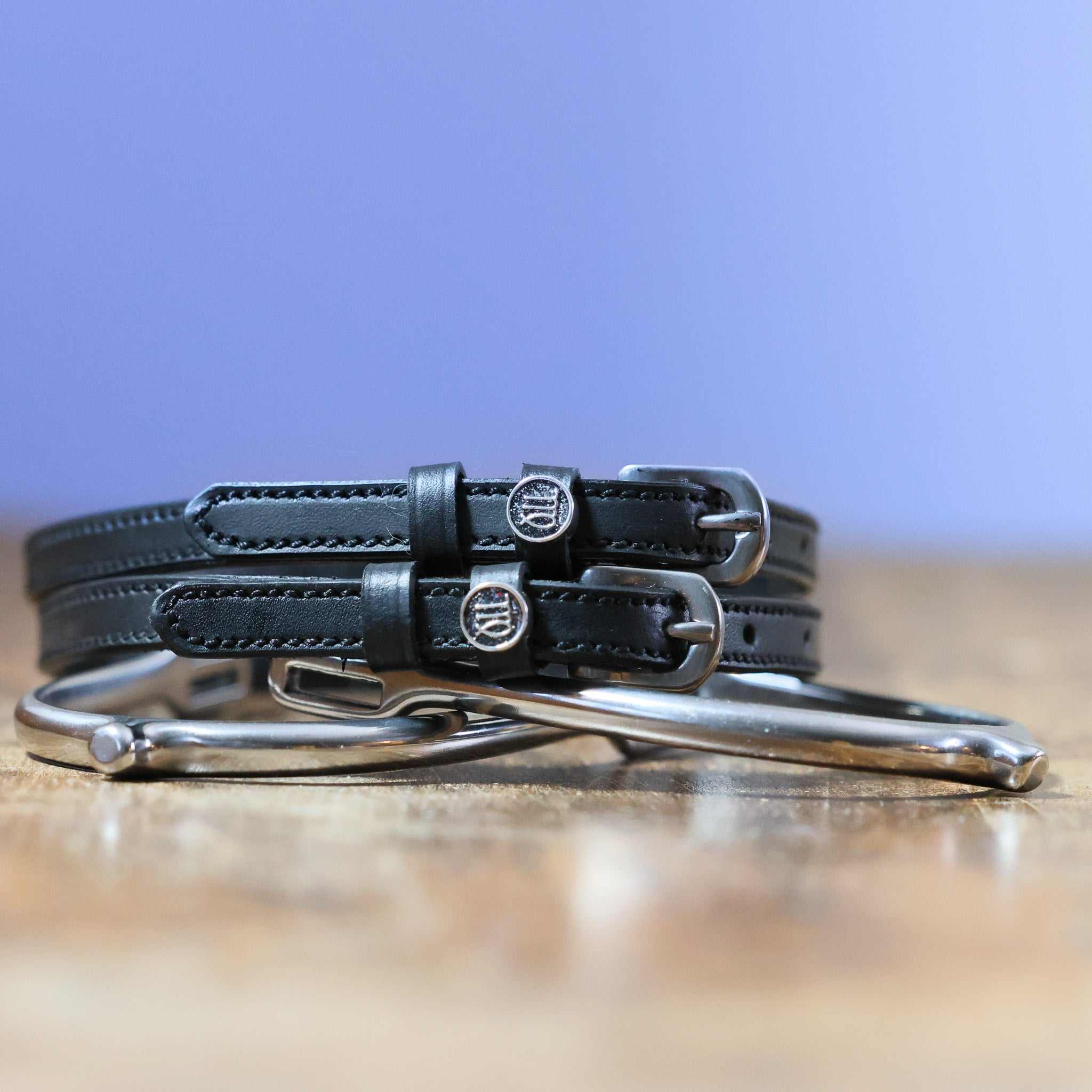 Virgo Spur Straps black leather with stainless steel buckles and custom charm on wooden surface