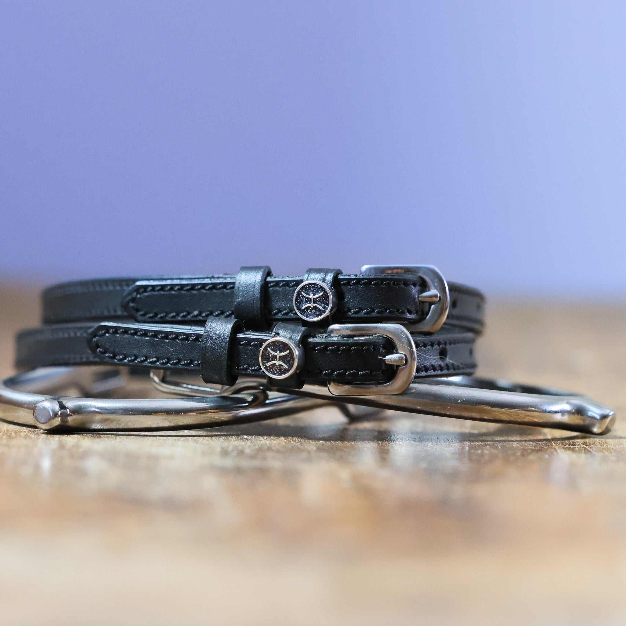 Black leather Pisces Spur Straps with stainless steel buckles and custom charm on wooden surface